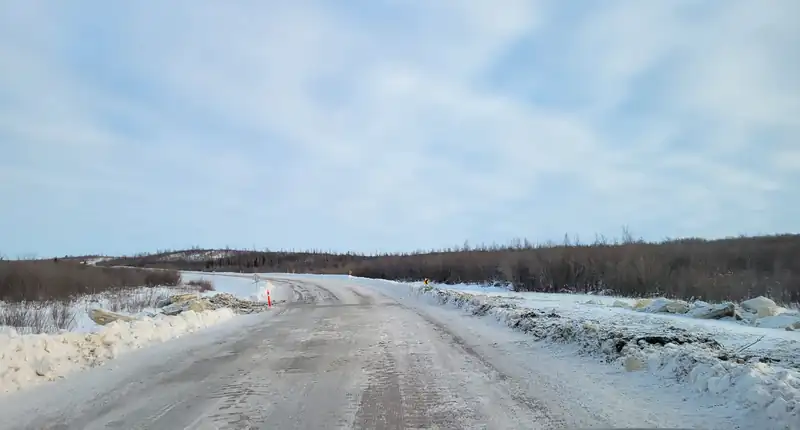The gravel Inuvik-Tuktoyaktuk Highway running straight across snowy tundra under a pale sky.